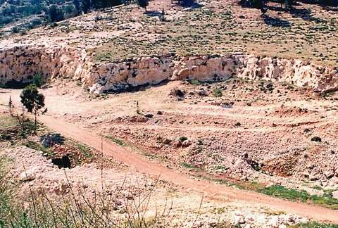 מחצבה נטושה, עם קיר סלע חשוף ודרך עפר על צלע הגבעה.
